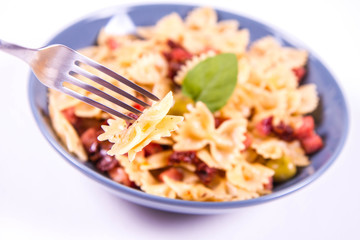 Farfalle pasta with sun dried tomato, ham and olives decorated with fresh mint eaten with a fork