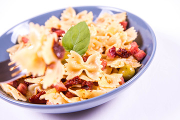 Farfalle pasta with sun dried tomato, ham and olives decorated with fresh mint eaten with a fork