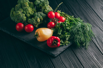 Fresh vegetables: cherry tomatoes, broccoli, pepper, dill, parsley on a dark wooden table. Recipe. Ingredients. Dietary food. Place under the text. View from above.