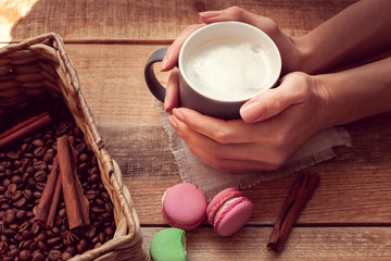 female hands holding a cup of coffee and macaroons