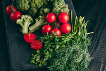 On a dark wooden table, fresh green broccoli, parsley, dill and cherry tomatoes for your health. Recipe. Ingredients. Dietary food. Place under the text. Top view.