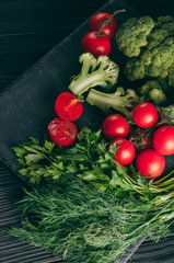 On a dark wooden table, fresh green broccoli, parsley, dill and cherry tomatoes for your health. Recipe. Ingredients. Dietary food. Place under the text. Top view.