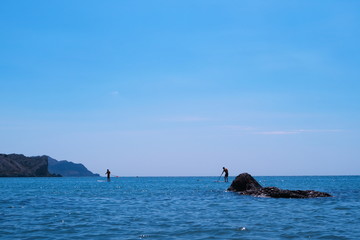 Fototapeta premium Walking along the sea while standing on a board with a paddle.