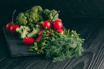 On a dark wooden table, fresh green broccoli, parsley, dill and cherry tomatoes for your health. Recipe. Ingredients. Dietary food. Place under the text. Top view.