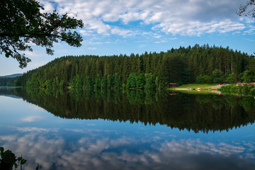 Fototapeta na wymiar Lake with Reflection on the Water and Trees in the background and Clouds on the sky in the bavarian forest