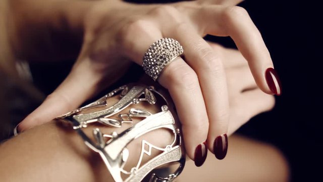 Close-up of beautiful female hands with red nails with gold big bracelet and diamond ring. Gold Jewelry for Women. Luxurious life. Advertising jewelry. In studio on black background.