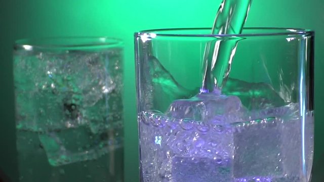 Soda water with bubbles pours into a glass with ice on a bright green background