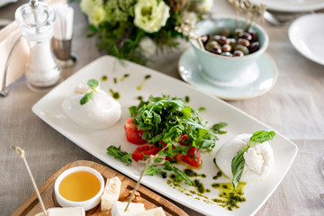 Italian Caprese salad. burrata cheese, tomatoes and basil herb leaves. Balsamic vinegar arranged on white plate