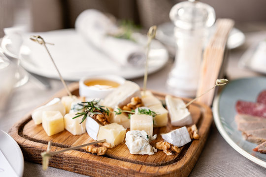 Cheese plate. Delicious cheese mix with walnuts, honey on wooden table. Tasting dish on a wooden plate. Food for wine.