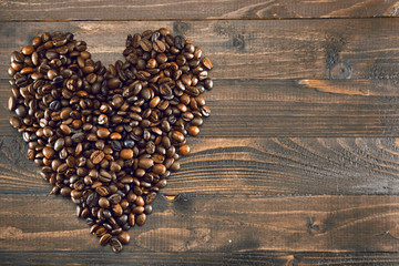 Grains of coffee in the shape of heart on a wooden background in the left part of the frame, space for text