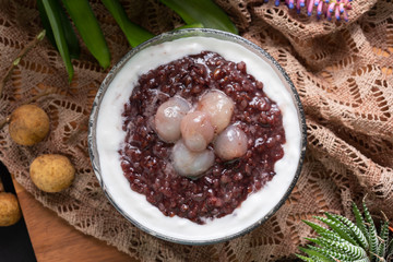 Close up soft sweet purple sticky rice pudding, Black Glutinous Rice, with longan and coconut cream on wooden table