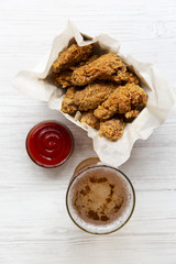 Chicken wings with ketchup, cold beer over white wooden background, top view. From above, overhead. Closeup.