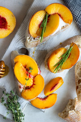 Baguette with peach, soft cheese, honey and rosemary served on a white wooden cutting board. Bruschetta or sandwich for a picnic. Fruit summer snack. Traditional italian food.