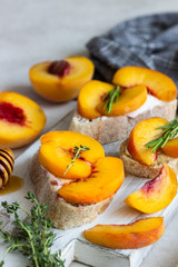 Naklejka na ściany i meble Baguette with peach, soft cheese, honey and rosemary served on a white wooden cutting board. Bruschetta or sandwich for a picnic. Fruit summer snack. Traditional italian food.