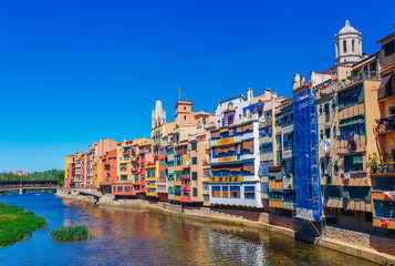 Fototapeta premium Colorful red, orange and yellow houses and bridge through river Onyar in Girona, Catalonia, Spain. Scenic ancient town. Famous tourist resort destination perfect place for holiday and vacation