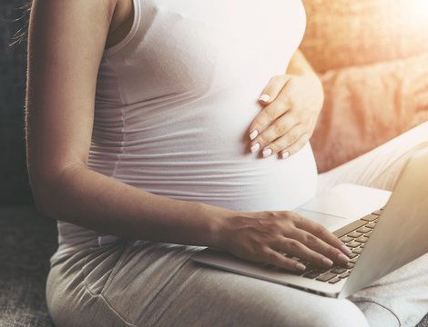 Pregnant Woman Using Laptop and Sitting on Sofa.