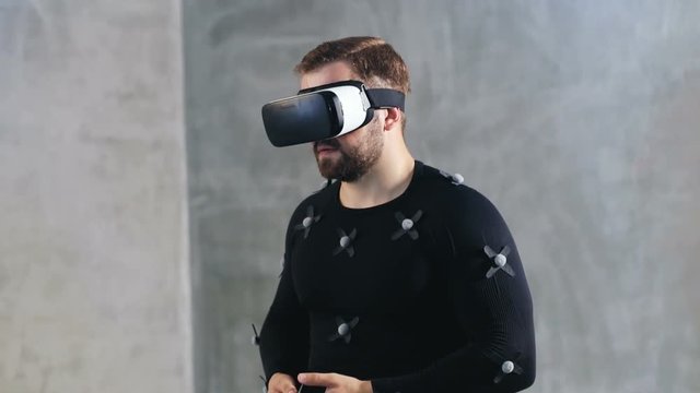 studio shoot of adult handsome man in motion-capture suit and virtual reality headset enjoying the experience of vr immersion hands gesturing smiling face optical motion capture systems industry