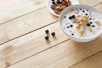 Fototapeta na wymiar Oatmeal porridgewith bananas, nuts, raisins, blueberries and milk on table on wooden background. Healthy breakfast and diet food. Top view