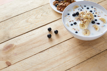 Oatmeal porridgewith bananas, nuts, raisins, blueberries and milk on table on wooden  background.  Healthy breakfast and diet food. Top view