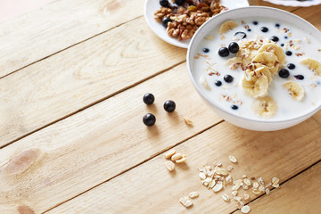 Oatmeal porridgewith bananas, nuts, raisins, blueberries and milk on table on wooden  background.  Healthy breakfast and diet food. Top view