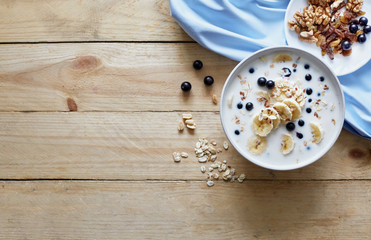 Oatmeal porridgewith bananas, nuts, raisins, blueberries and milk on table on wooden  background.  Healthy breakfast and diet food. Top view