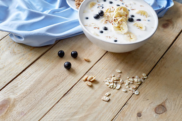 Fototapeta na wymiar Oatmeal porridgewith bananas, nuts, raisins, blueberries and milk on table on wooden background. Healthy breakfast and diet food.