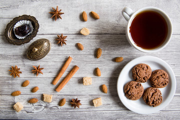 Chocolate cookies with black tea, nuts, almonds, anise stars, brown sugar, dates and cinnamon sticks on wooden background, top view, Christmas concept.