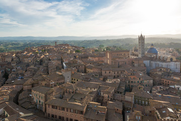 Aerial and top view scenery of old ancient Tuscany region town and medieval brick buildings with green range mountain landscape background in Siena, Italy  