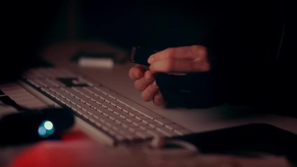 Hacker hands holding memory card, slowly moving it from point A to point B, keyboard in the background. In darkness with red light. - Powered by Adobe