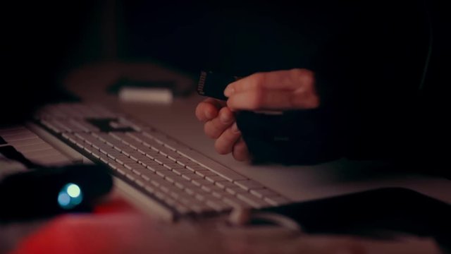 Hacker hands holding memory card, slowly moving it from point A to point B, keyboard in the background. In darkness with red light.