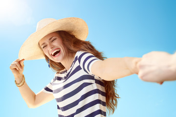 happy young woman holding hand of man against blue sky