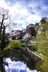 Fototapeta na wymiar Looking Down the Alzette River Lined with Spring Trees and Flowers as It Flows through the Village of Grund in Luxembourg City, Luxembourg