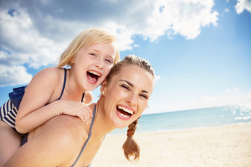 smiling modern mother and daughter in beachwear on seashore