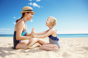 happy young mother and daughter in swimwear on seacoast playing