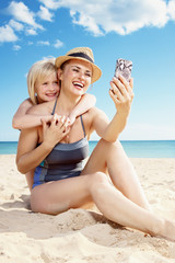 smiling mother and child taking photo with smartphone on beach