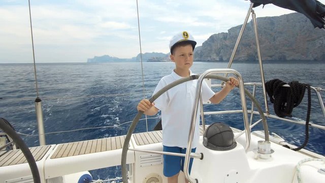 Litle children captain at the helm controls of a sailing yacht during race.