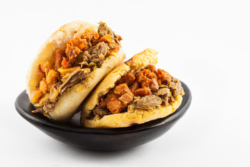 Arepas filled with shredded beef and pork rind served in a black ceramic dish on white background