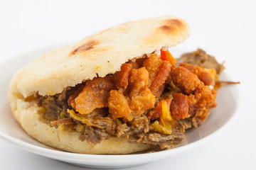Arepas filled with shredded beef and pork rind served in white dish on white background