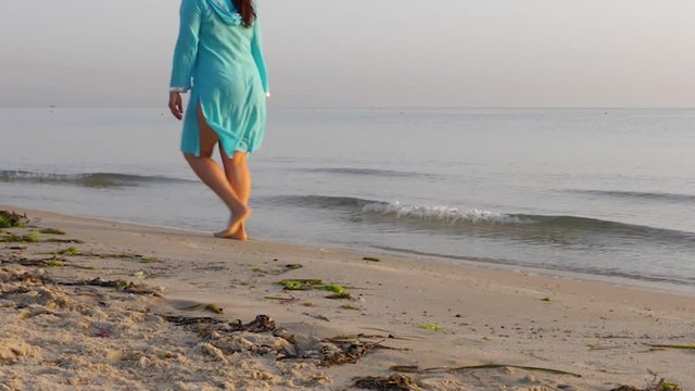 Barefoot woman in blue walking on sandy beash near the sea