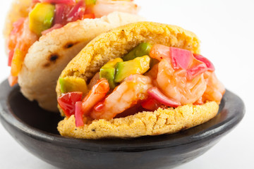Arepas filled with shrimp ceviche served in a black ceramic dish on white background