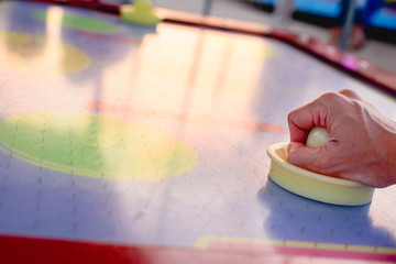 Hand holding a stick to hit disc in the table air hockey game.