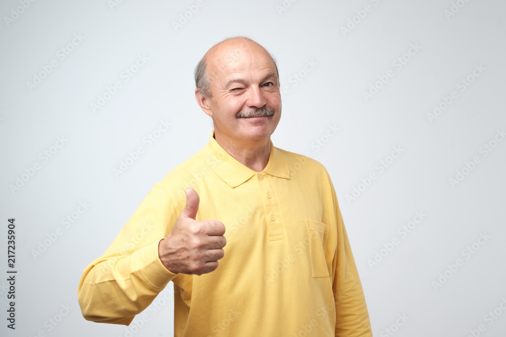 Poster handsome, bald man with his thumb up in sign of optimism on white background