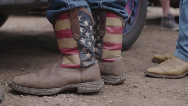 Cowboy’s Boot With American Flag Patter, Mud and Car in Background