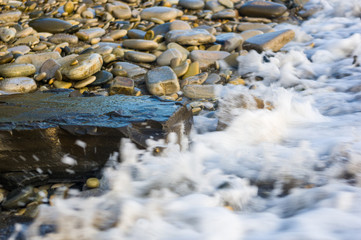 pebble stones on the sea beach, the rolling waves of the sea with foam