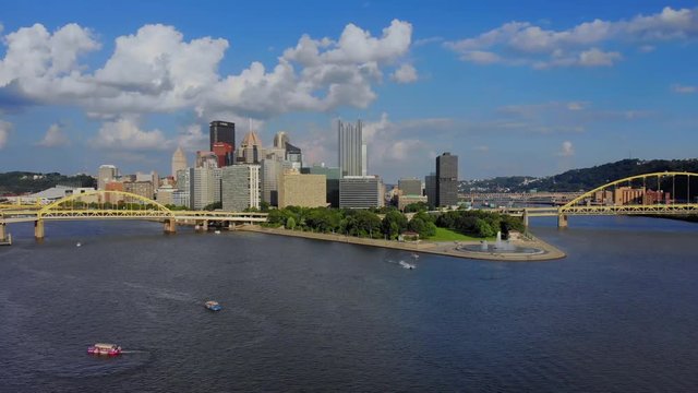 A slow reverse aerial establishing wide shot of the skyline of Pittsburgh, Pennsylvania on an early summer evening. Ducky tour boats and jet skis in the river below.  	