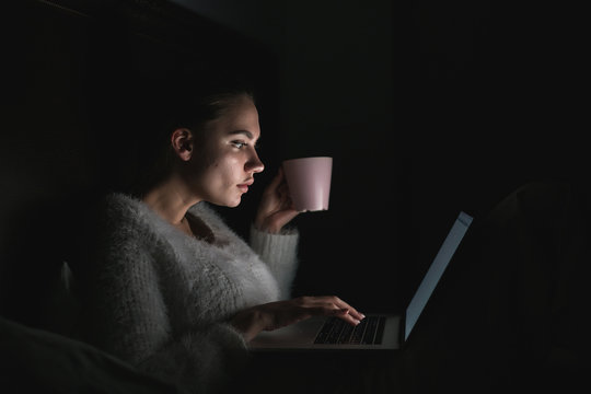 serious young girl working on laptop late at night, drinking coffee