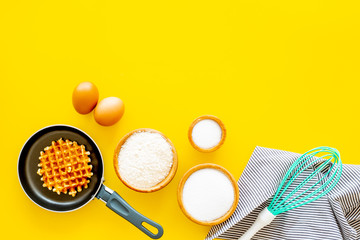 Ingredients for belgian waffles. Eggs, flour, sugar near waffle on pan, whisk for whipping on yellow background top view copy space