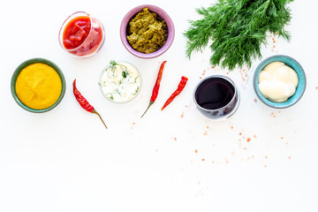 Set of sauces. Ketchup, mayonnaise, mustard, soy sauce, barbecue sauce, pesto, mustard, sour near chili pepper and greenery on white background top view copy space