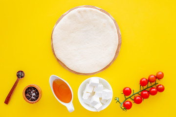 Ingredients for cooking vegetarian pizza. Rolled pizza dough, cherry tomatoes, olive oil, cheese mozzarella, spices on yellow background top view mockup copy space