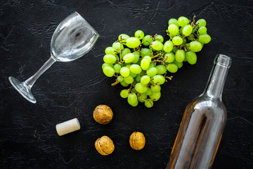 Composition with wine. Open white wine bottle, bunch of grapes, nuts, cork, wine glass on black background top view